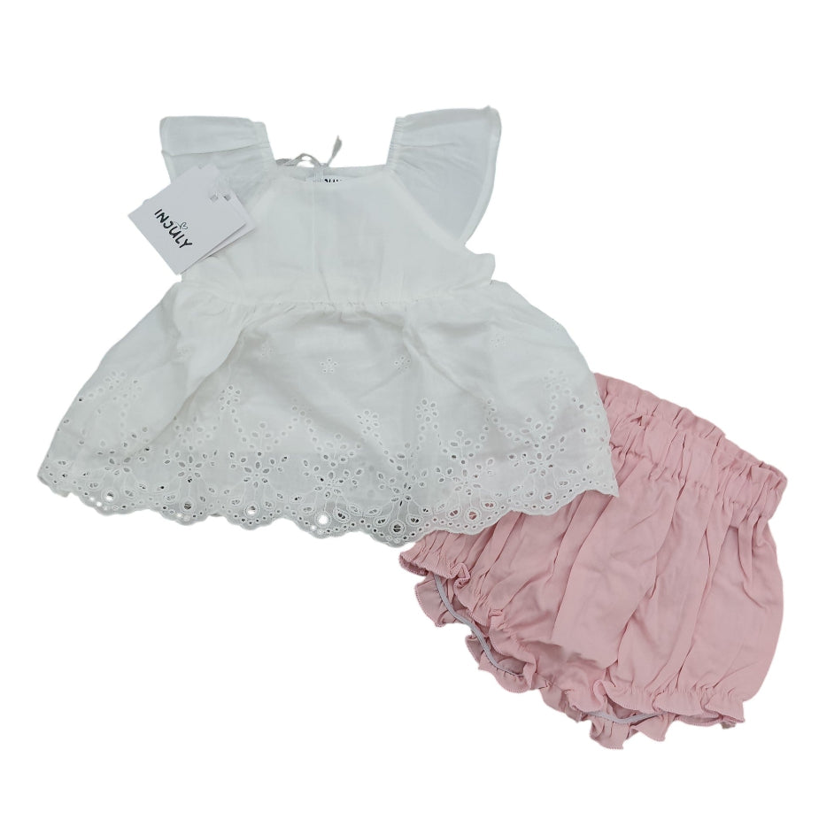 Completo estivo da neonata InJuly composto da blusa smanicata bianca stile impero con ricami in pizzo Sangallo e shorts culotte rosa a sbuffo su sfondo bianco.